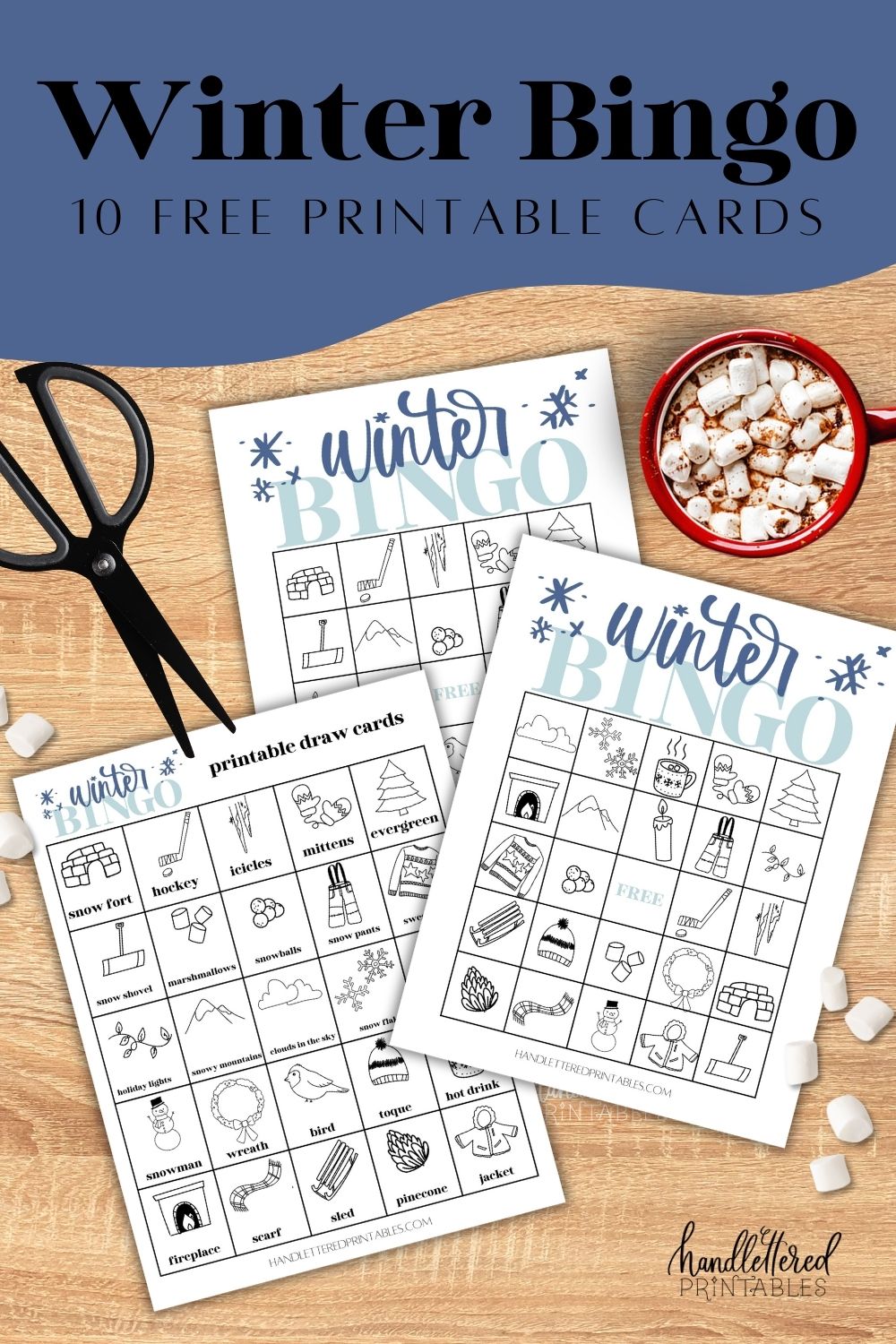 Winter themed bingo styled on wooden table with black scissors, cup of hot cocoa and lots of mini marshmallows. tet over reads winter bingo 10 free printable cards
