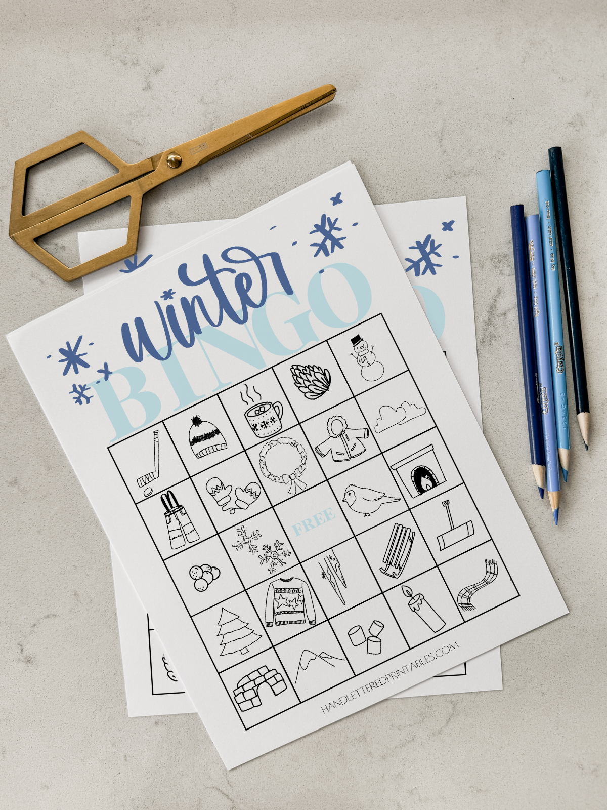 Winter Bingo cards printed on marble countertop with gold scissors and blue pencil crayons
