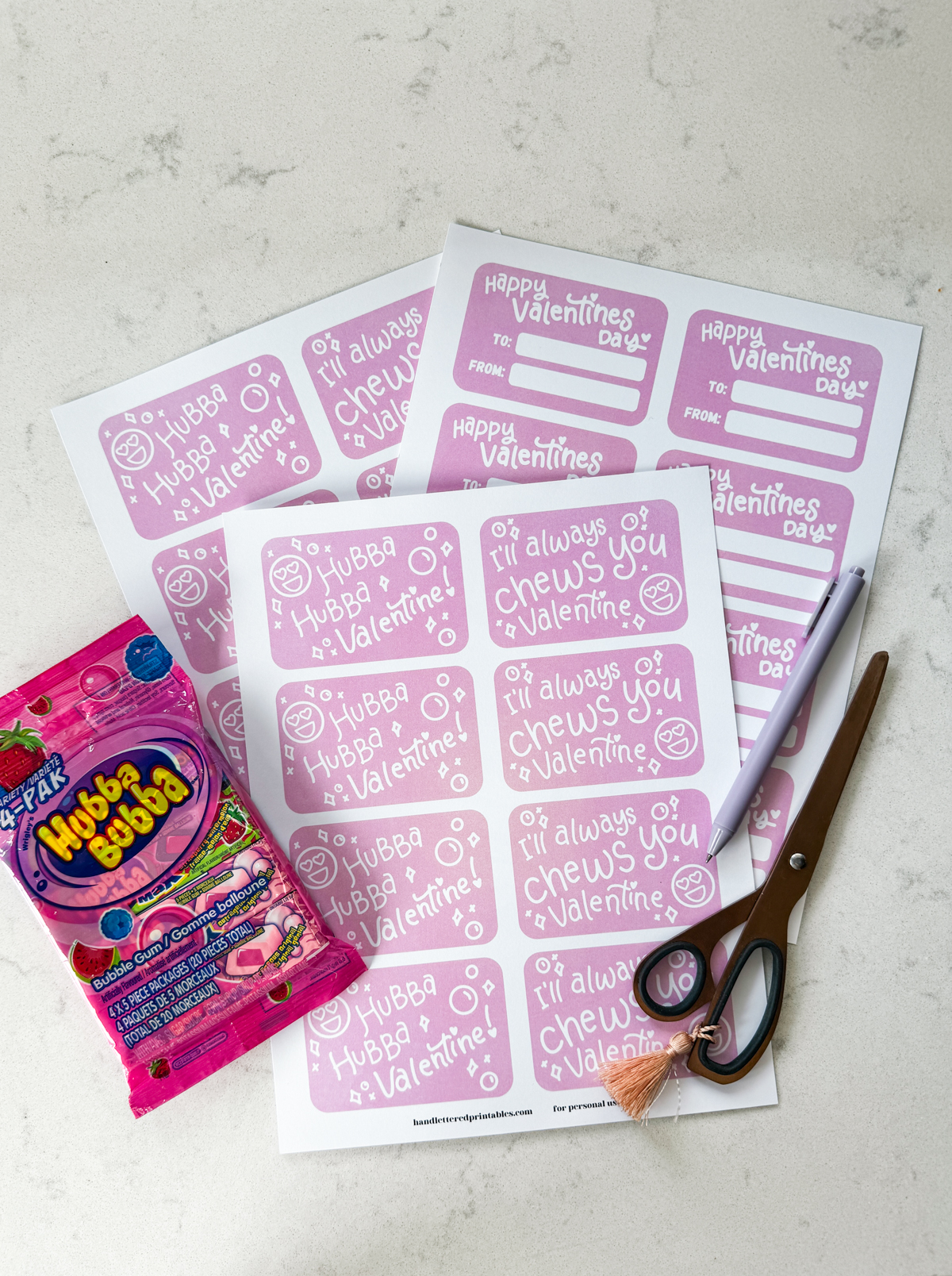 image of printed valentines cards (showing front and back) with a bubble gum theme, styled on marble countertop with scissors, pen and hubba bubba gum. valentines read 'hubba hubba valentine!' and 'I'll always chews you, valentine'