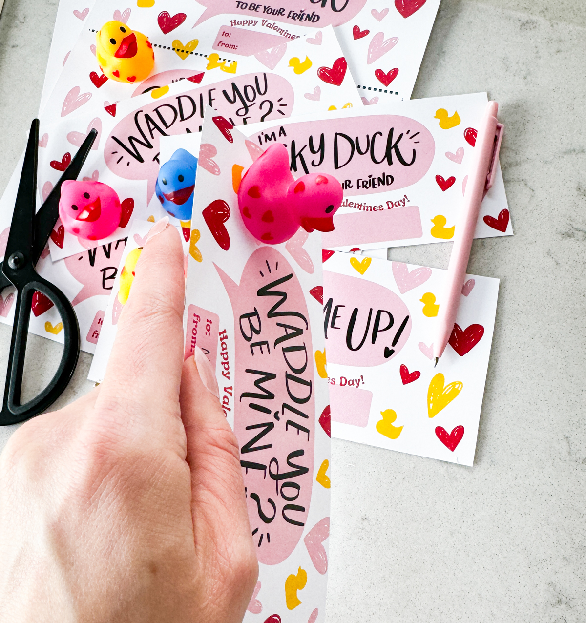 duck themed printable valentines day cards. card shown reads: waddle you be mine, hey valentine you quack me up and lucky to be your friend- all with a small happy valentines day. shown with rubber duckies affixed to valentine with doublesided tape (pink)