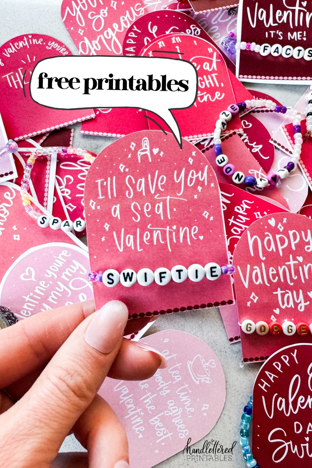 text reads: taylor swift themed valentines day cards printed and cut to size (pink and deep burgundy color with white hand lettered song lyrics) shown on marble countertop with beaded friendship bracelets. held valentine reads: i'll save you a seat, valentine with a 'swiftie' bracelet.