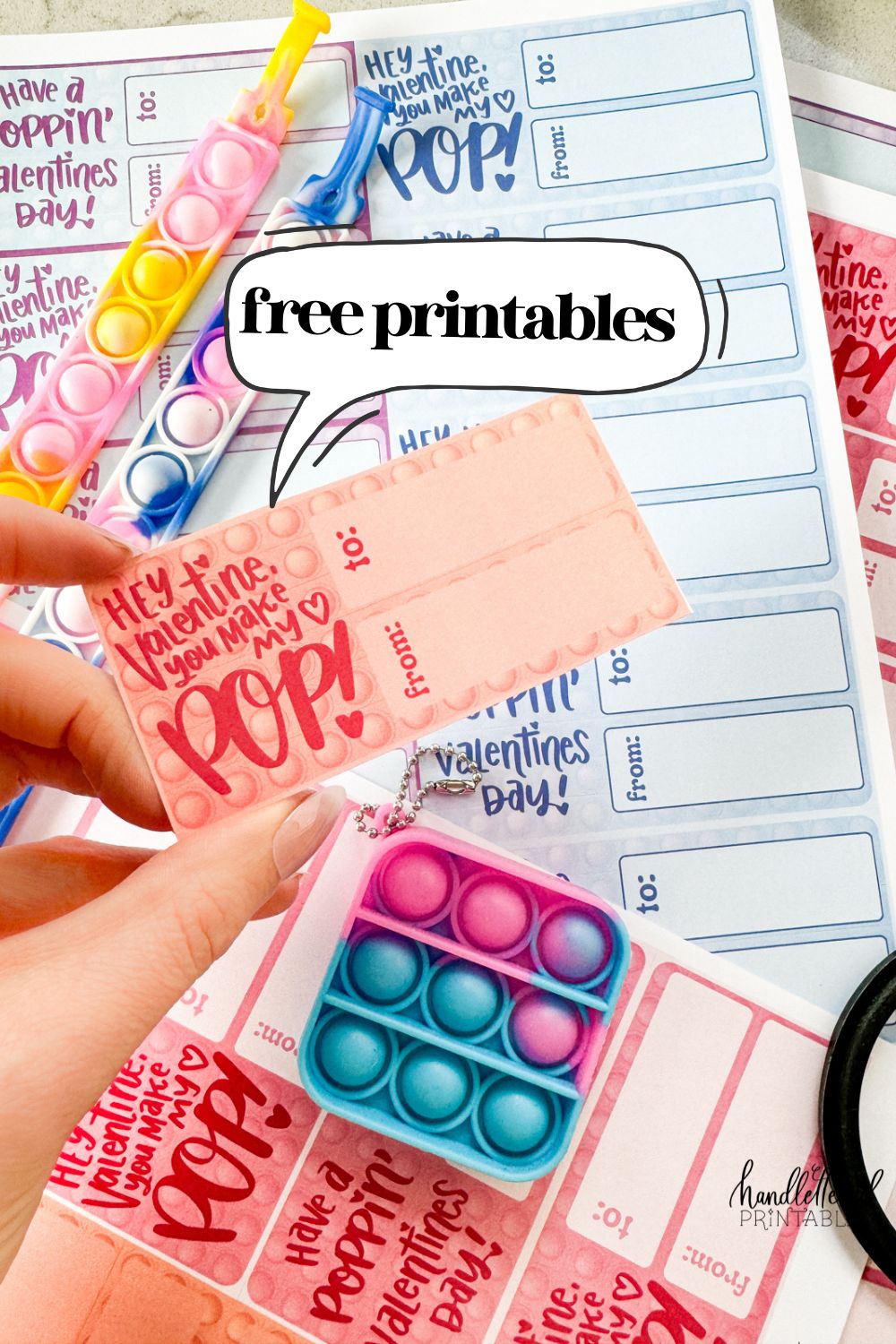 text reads: free printables pop it themed valentines cards printed and styled with popits. 4 color schemes with two sentiments: hey valentine, you make my heart pop' (held in photo) and 'have a poppin valentines day'.