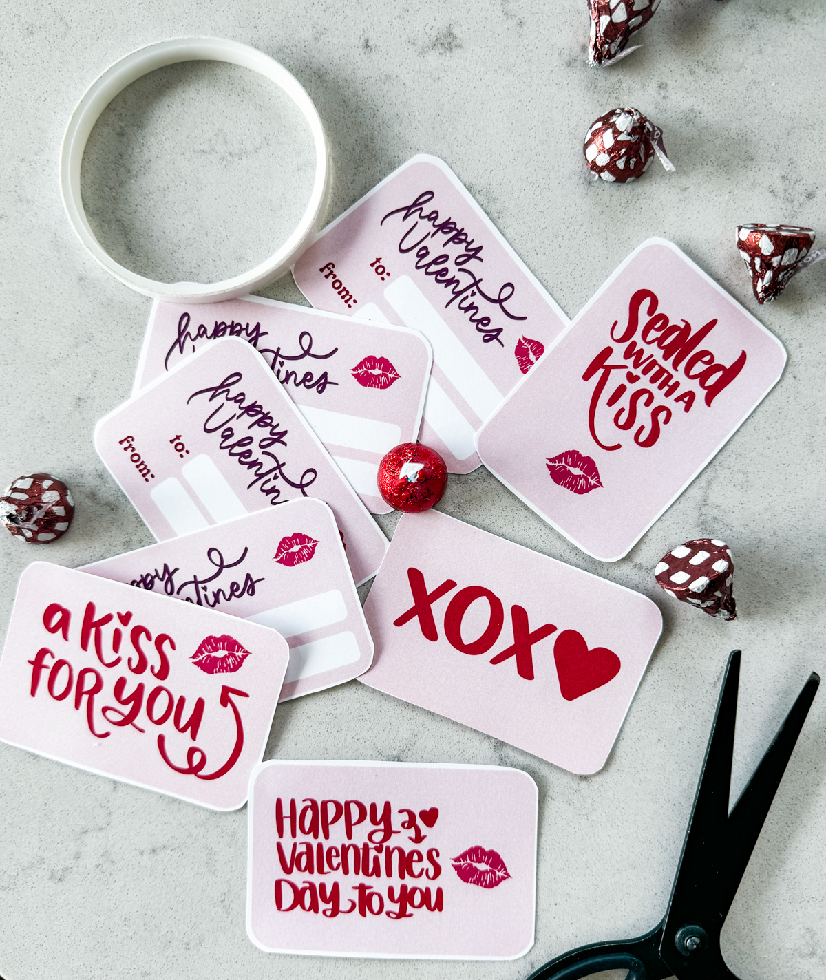 image of printable valentine cards cut to size and styled with scissors, chocolate kisses and double sided tape, valentines cards read: a kiss for you, xoxo, happy valentines day to you, sealed with a kiss
