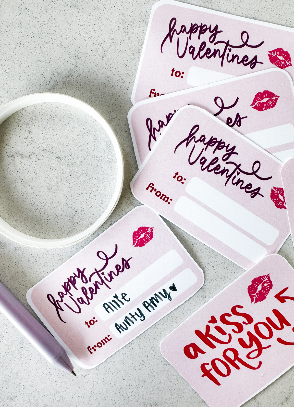 image of pink valentines cards cut to size with rounded corners. purple hand lettering reads 'happy valentines' with a kiss and space for the to and from names, front of valentine shown reads 'a kiss for you'