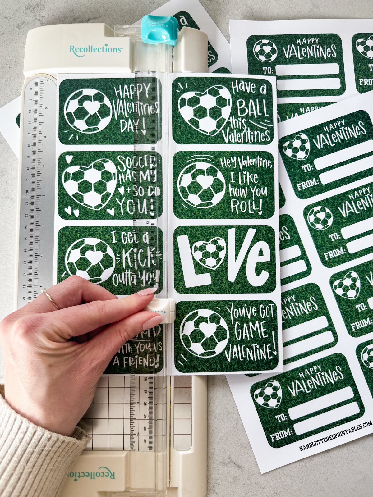 image shows soccer themed valentines printed in full sheets, using a small paper cutter to cut to size valentines have a heart shaped soccer ball and a soccer ball with a heart on it and a grass background. valentines puns and sentiments include: happy valentines day, have a ball this valentines, hey valentine i like how you roll, soccer has my heart and so do you, i get a kick outta you, love (with a heart soccerball as the o), you've got game valentine, and i really scored with you as a friend reverse reads 'happy valentines' with room for to and from names. soccer/ american football