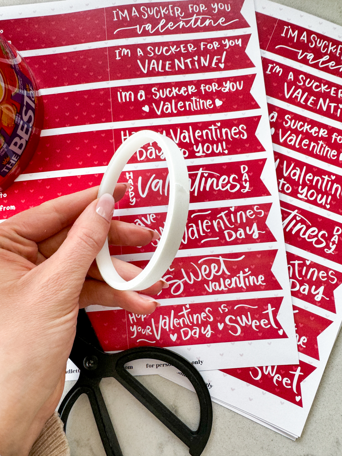 image of roll of double sided tape held over printed sucker tags for valentines day