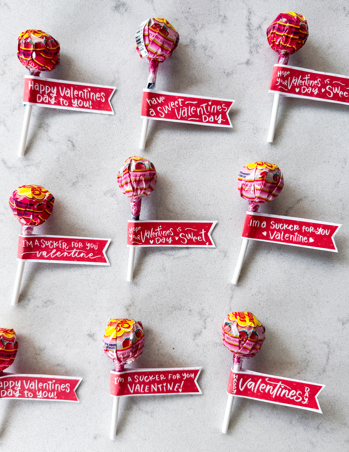Free printable valentines tags for suckers shown on suckers, 9 in total assembled like little flags on the sucker sticks