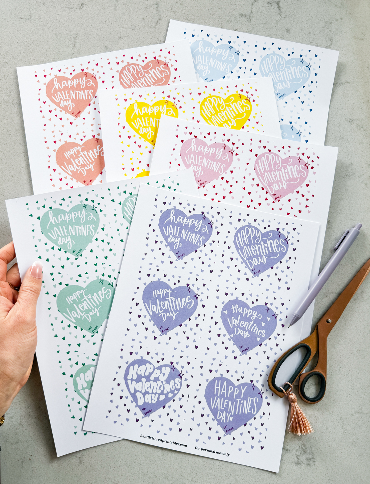 happy valentines day hand lettered valentines cards free printable shown printed off but not yet cut to size. 6 color schemes available, shown on marble countertop with scissors and pen