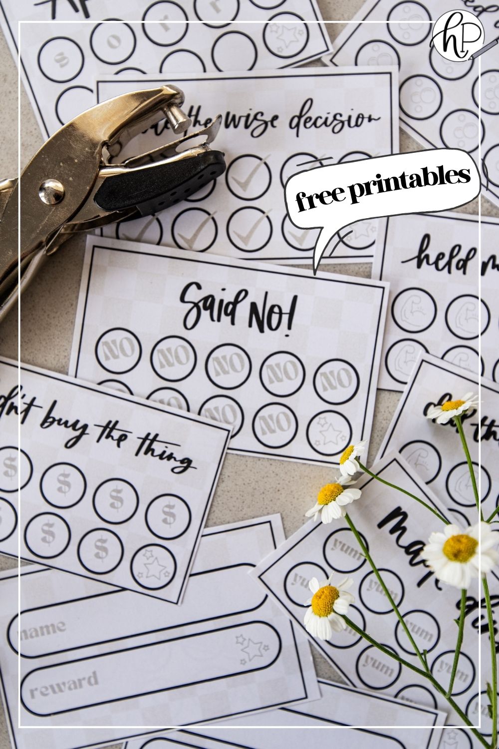 image of printed punch cards for adults, cut to size on countertop with hole punch and cut flowers punch cards have a soft checkerboard background with hand lettered goals like 'said no!', 'didn't buy the thing' and 'made the wise decision' text bubble reads 'free printables'