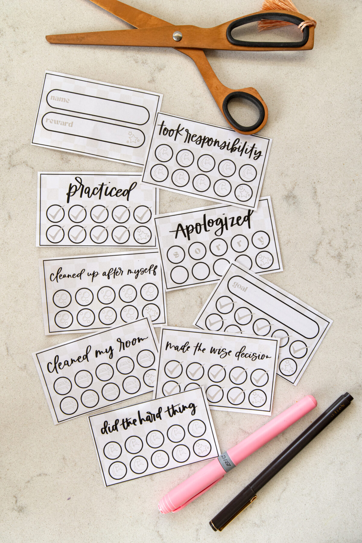 image of printed punch cards for kids, cut to size with scissors punch cards have a soft checkerboard background with hand lettered goals like 'practiced', 'took responsibility', 'apologized', 'cleaned up after myself' and 'made the wise decision'