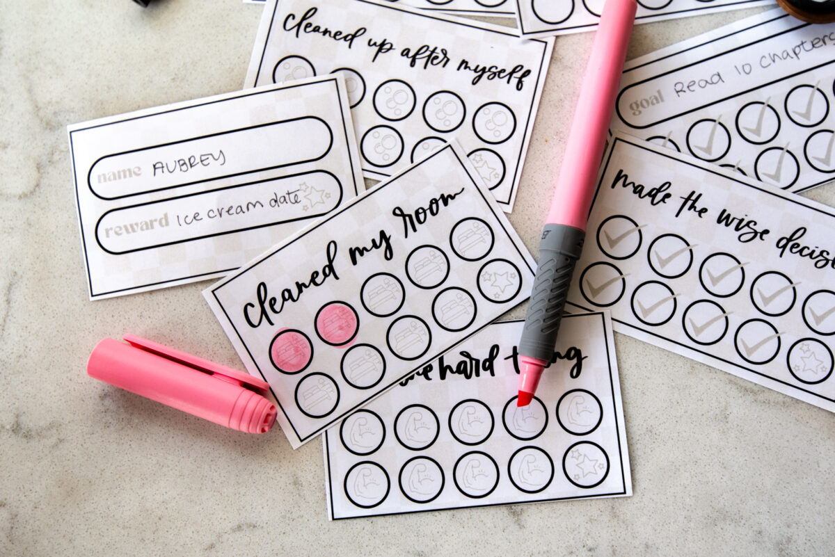 image of printed punch cards for kids, cut to size with scissors punch cards have a soft checkerboard background with hand lettered goals like 'practiced', 'took responsibility', 'apologized', 'cleaned up after myself' and 'made the wise decision' two punches colored in with a highlighter