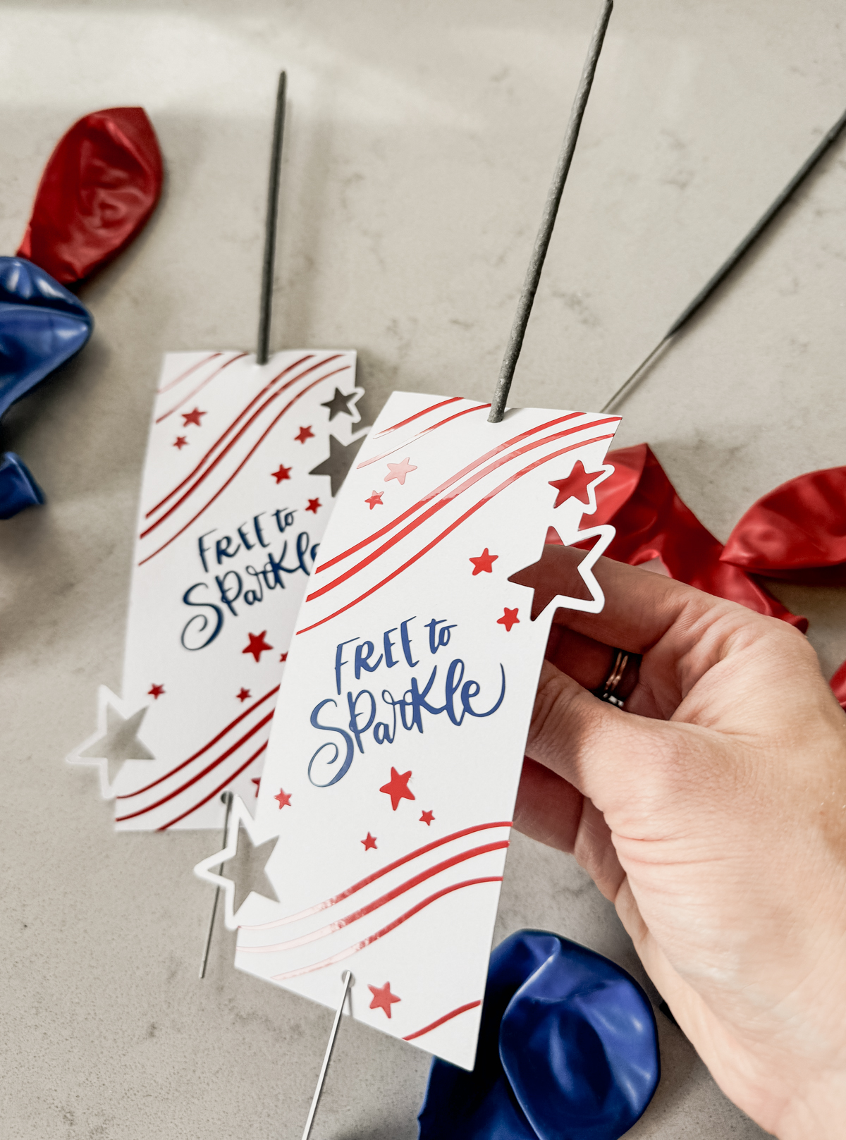 image of fourth of july sparklers holders free svg file with 3 layers, shown assembled with sparklers, being held by hand above a countertop with red and blue balloons