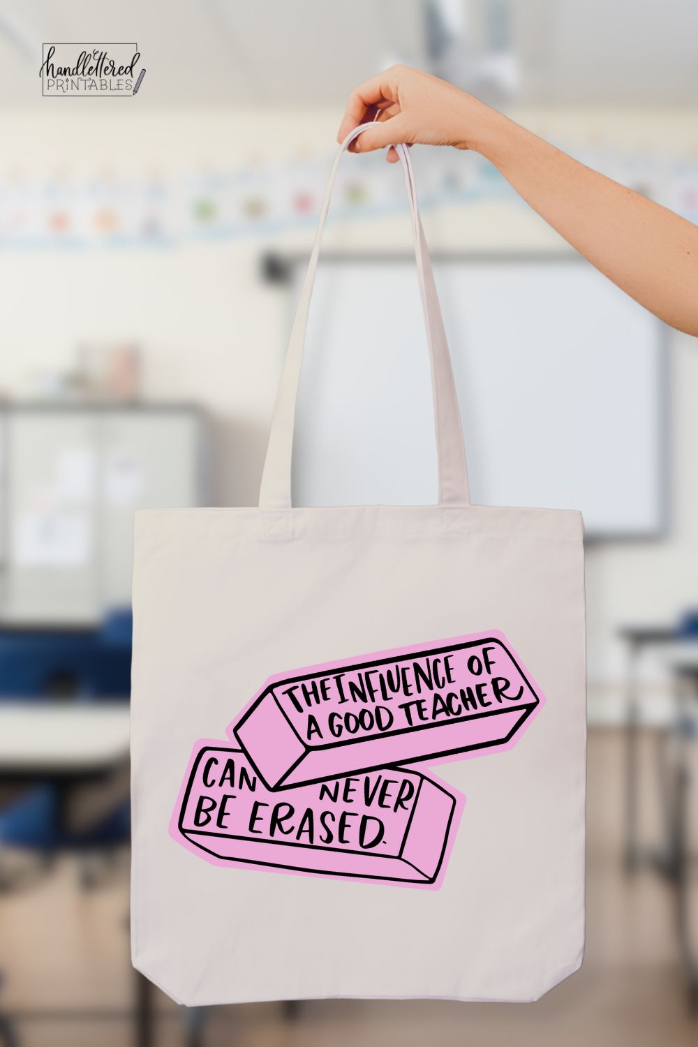 'The influence of a good teacher can never be erased' hand lettered SVG design in black iron on vinyl with pink background on tote bag held in front of classroom